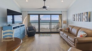 Een woonkamer met uitzicht op de oceaan, een plafondventilator, een bank, een salontafel en een eettafel.