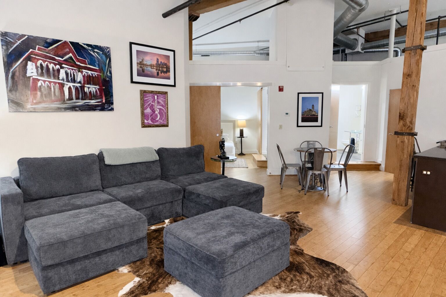 Una sala de estar moderna con un sofá seccional gris, una mesita y un comedor con sillas de metal.