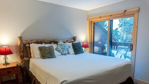 A bedroom with a large bed, two bedside tables, a nightstand, and a window with a view of the outdoors. - Walk to Skiing, Hiking and Main Street! (Breckenridge)