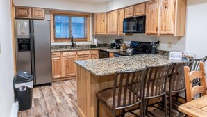 A kitchen with wooden cabinets, a stainless steel refrigerator, a microwave, and a granite countertop. - Walk to Skiing, Hiking and Main Street! (Breckenridge)