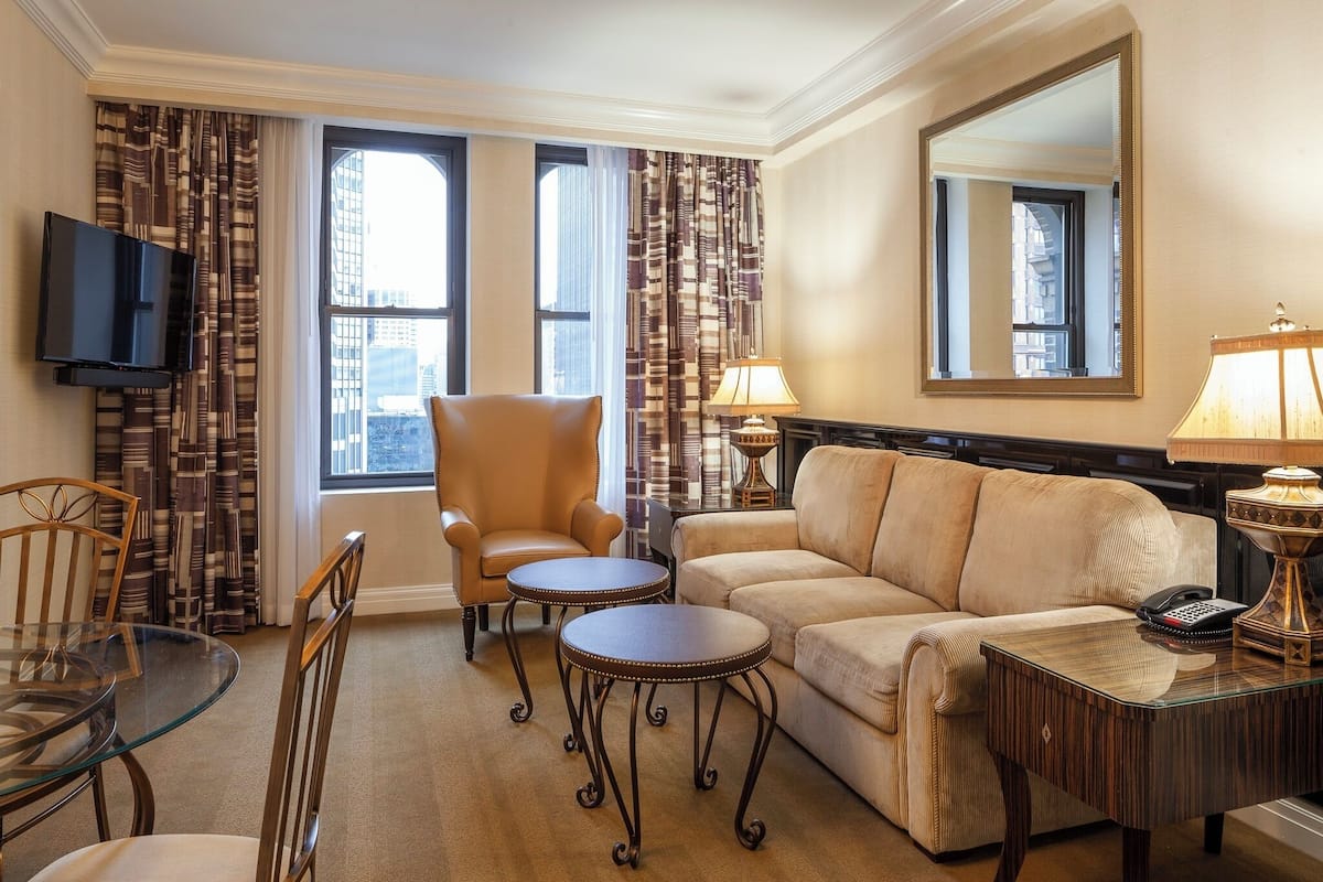 Une chambre d’hôtel équipée d’un canapé, d’un fauteuil, de deux petites tables, d’une télévision et d’une lampe.