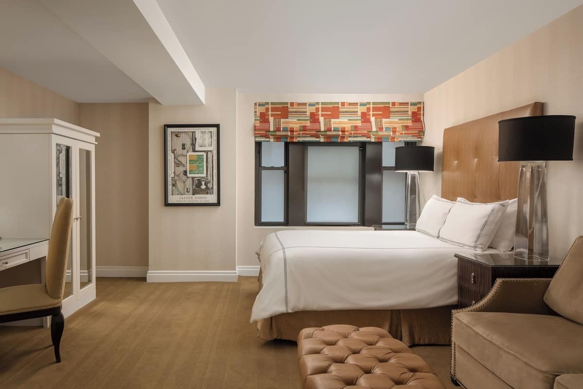 Une chambre d’hôtel avec un lit, un bureau, une chaise, une lampe et un tableau encadré au mur.