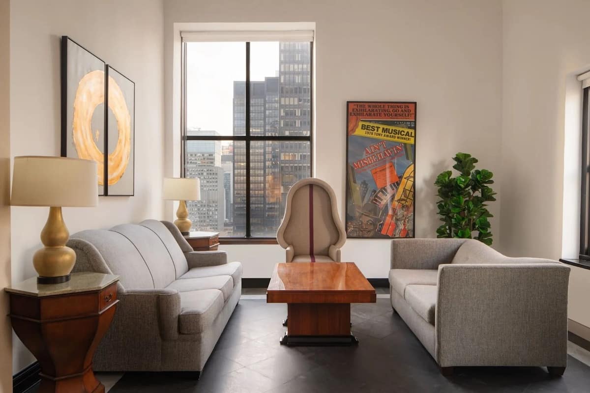 Un salon moderne avec un canapé, des fauteuils, une table basse et une grande fenêtre donnant sur la ville.