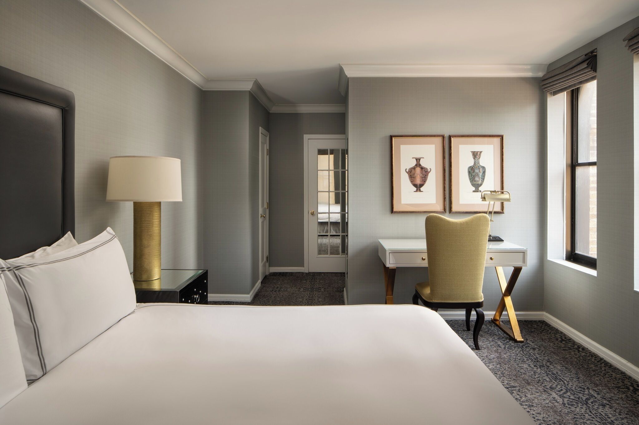 Camera d'albergo con un letto grande, una scrivania, una sedia, una lampada e due quadri appesi al muro.