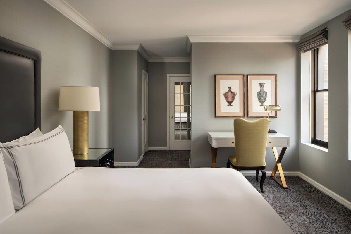 Een hotelkamer met een groot bed, een bureau, een stoel, een lamp en twee ingelijste foto's aan de muur.