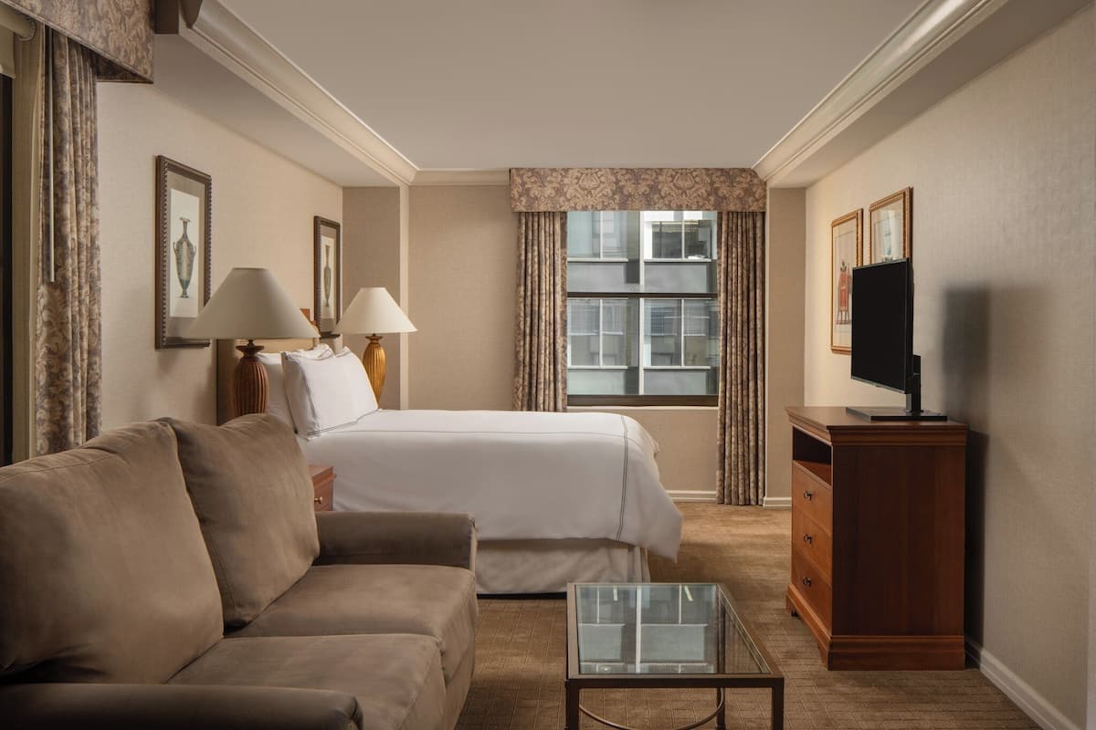 Une chambre d’hôtel avec un lit, un canapé, une télévision et une petite table.