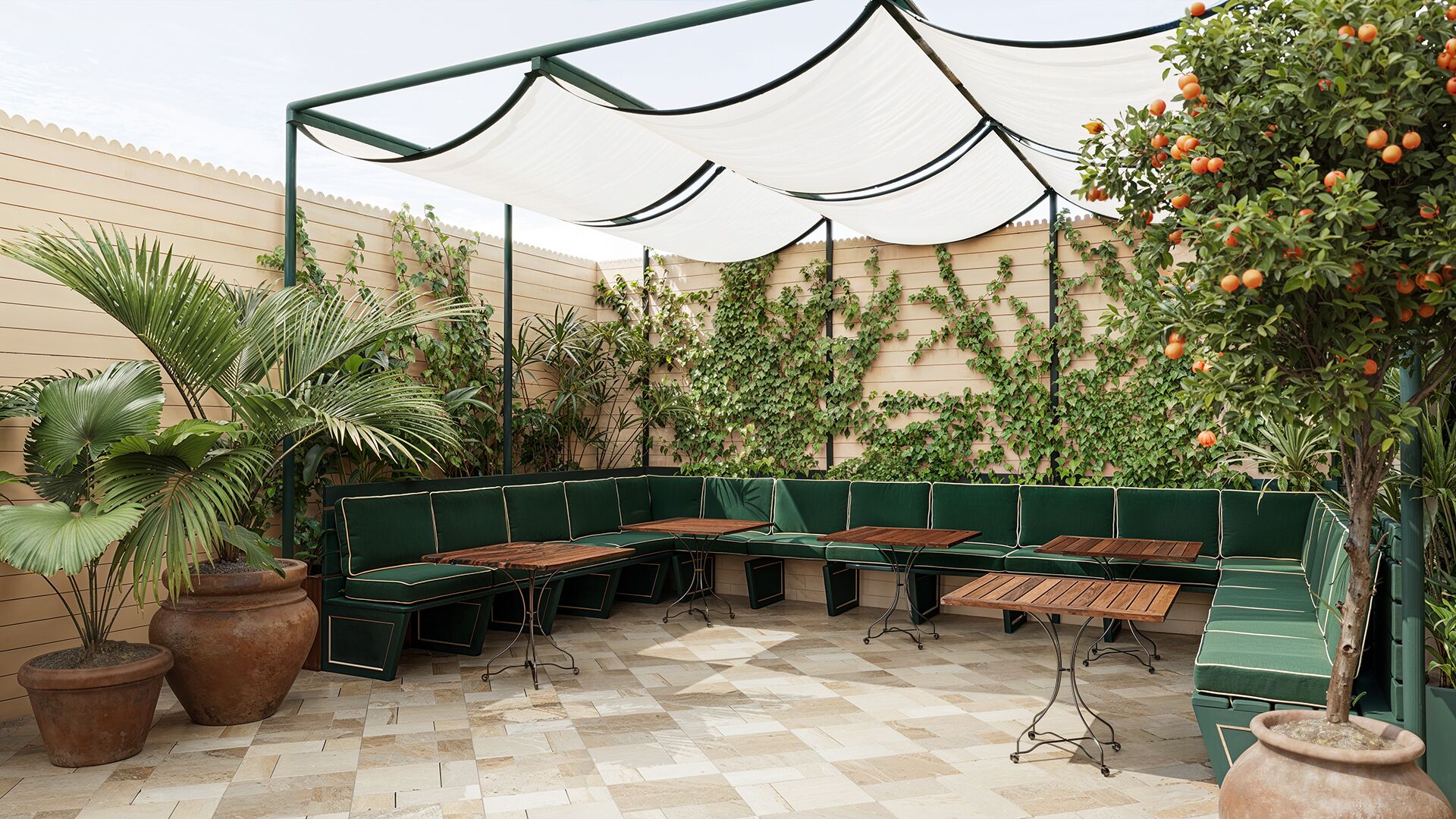 An outdoor seating area with a green bench, potted plants, and a tiled floor.