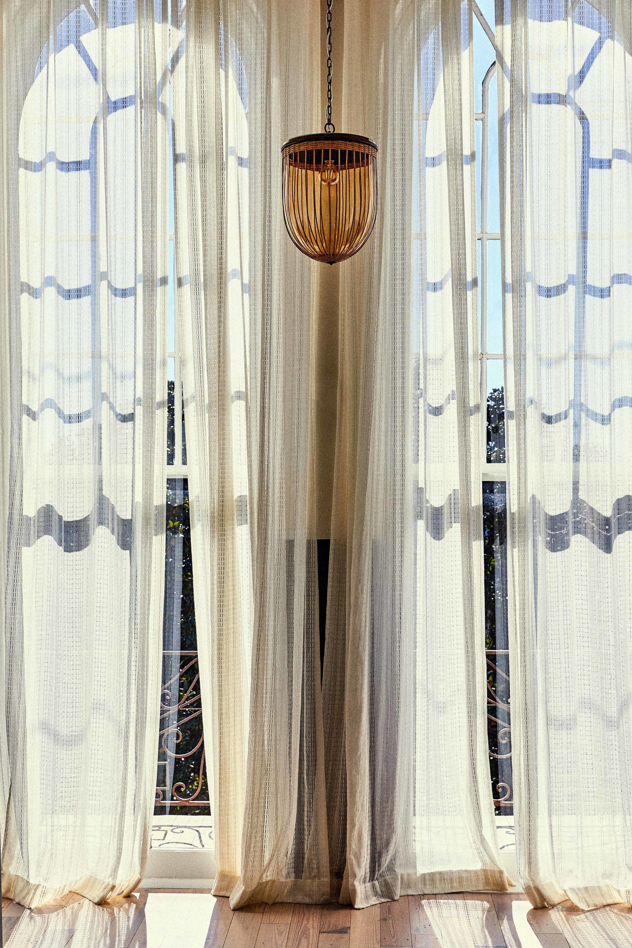 A room with sheer curtains, a hanging light fixture, and a view through the window.