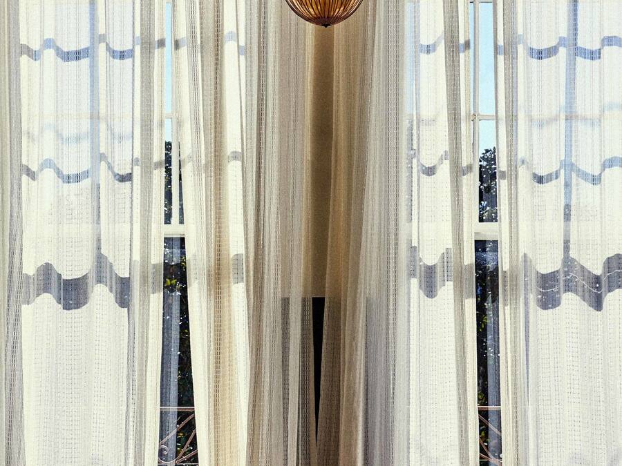 A room with sheer curtains, a hanging light fixture, and a view through the window.