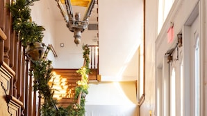 A grand staircase with a wooden railing, decorated with greenery and a lantern. A bench is placed at the bottom of the stairs. - Hotel Peter and Paul, an Ash Hotel (New Orleans)