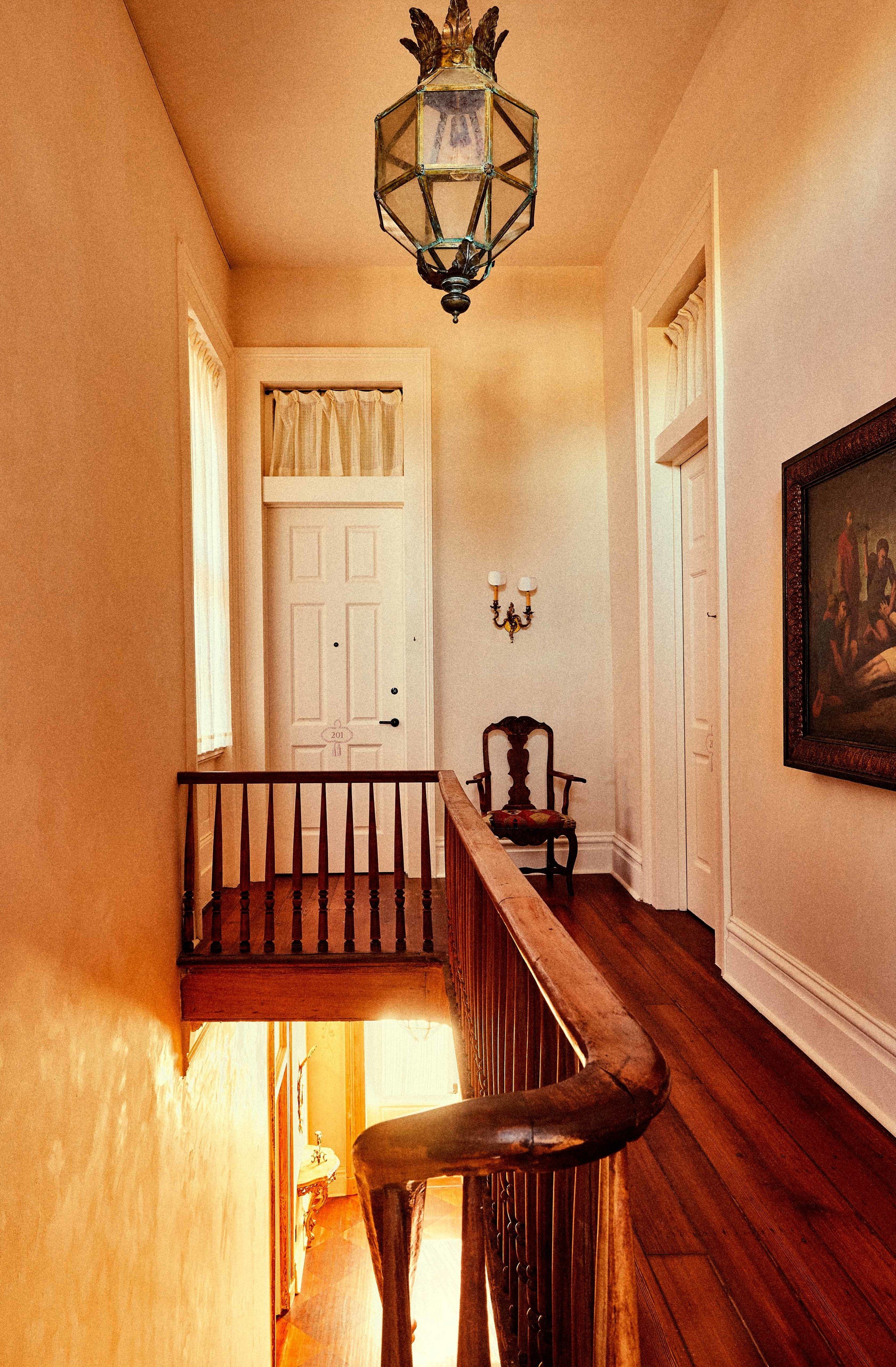 A hallway with a wooden staircase, a white door, a wall-mounted light fixture, and a framed painting.