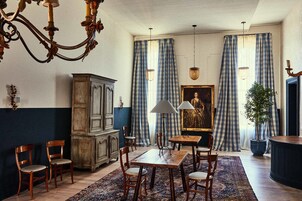 A dining area with a wooden table and chairs, a chandelier, and a large painting on the wall.