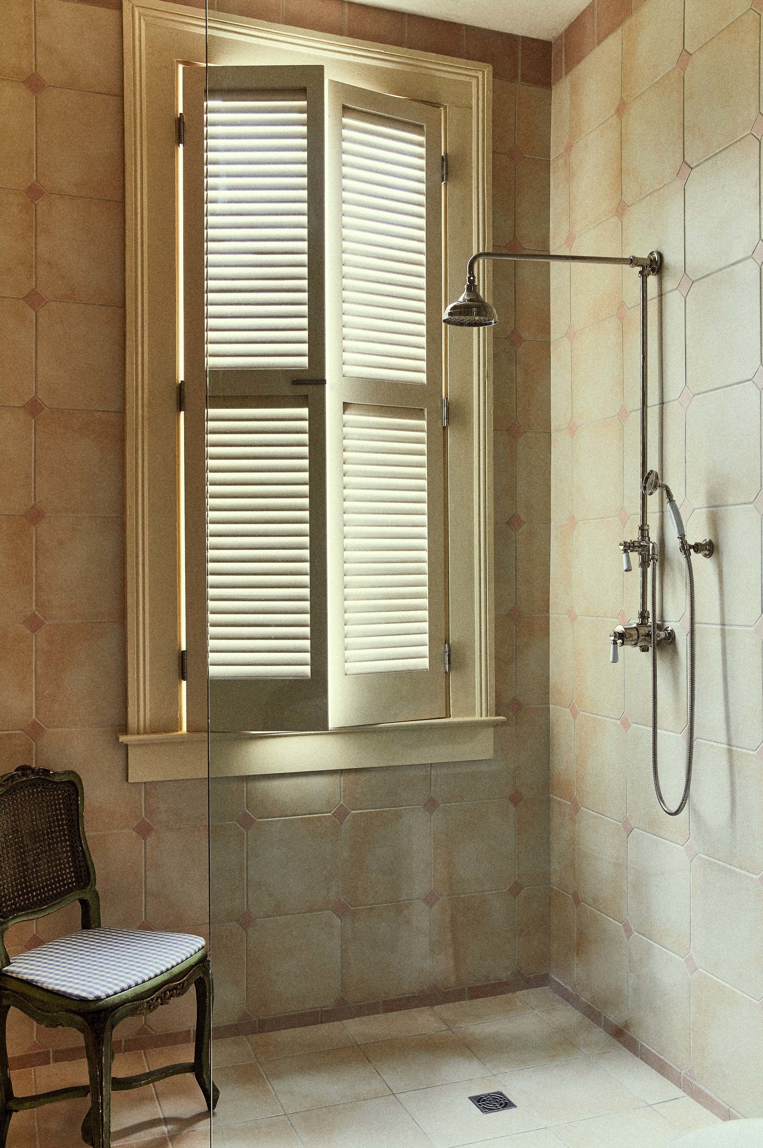 Een badkamer met een douche, een stoel en een raam met luiken.