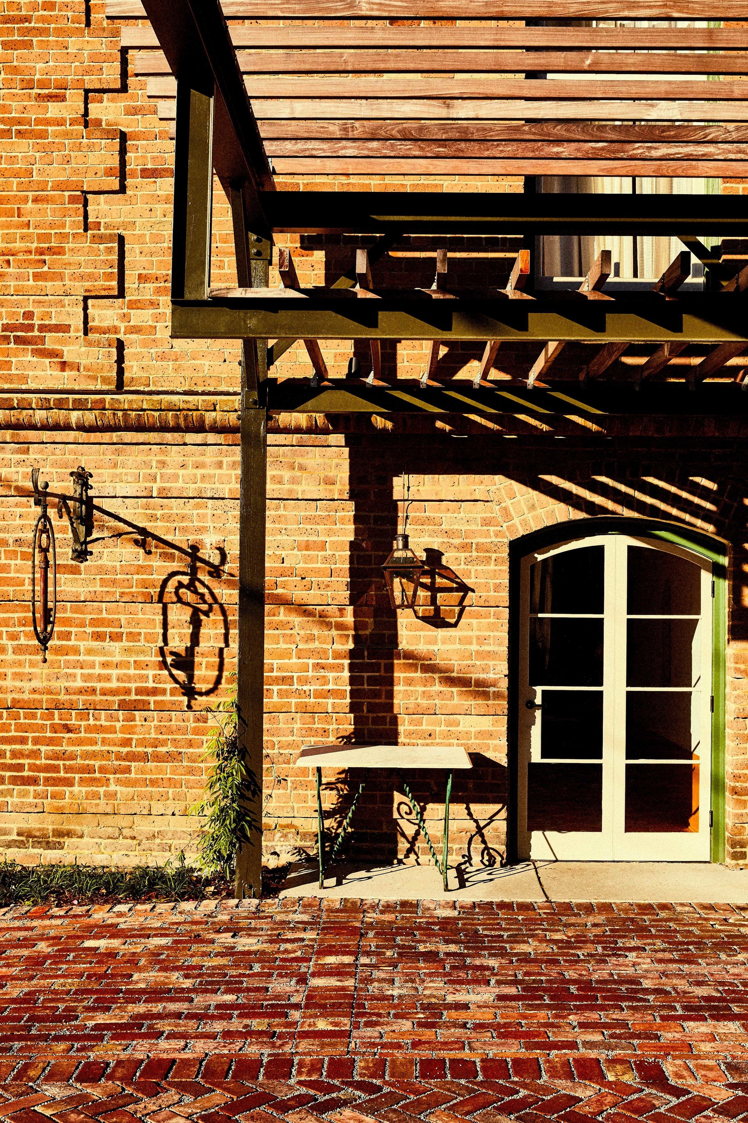 A brick building with a wooden pergola, a bicycle hanging on the wall, and a door with a green frame.