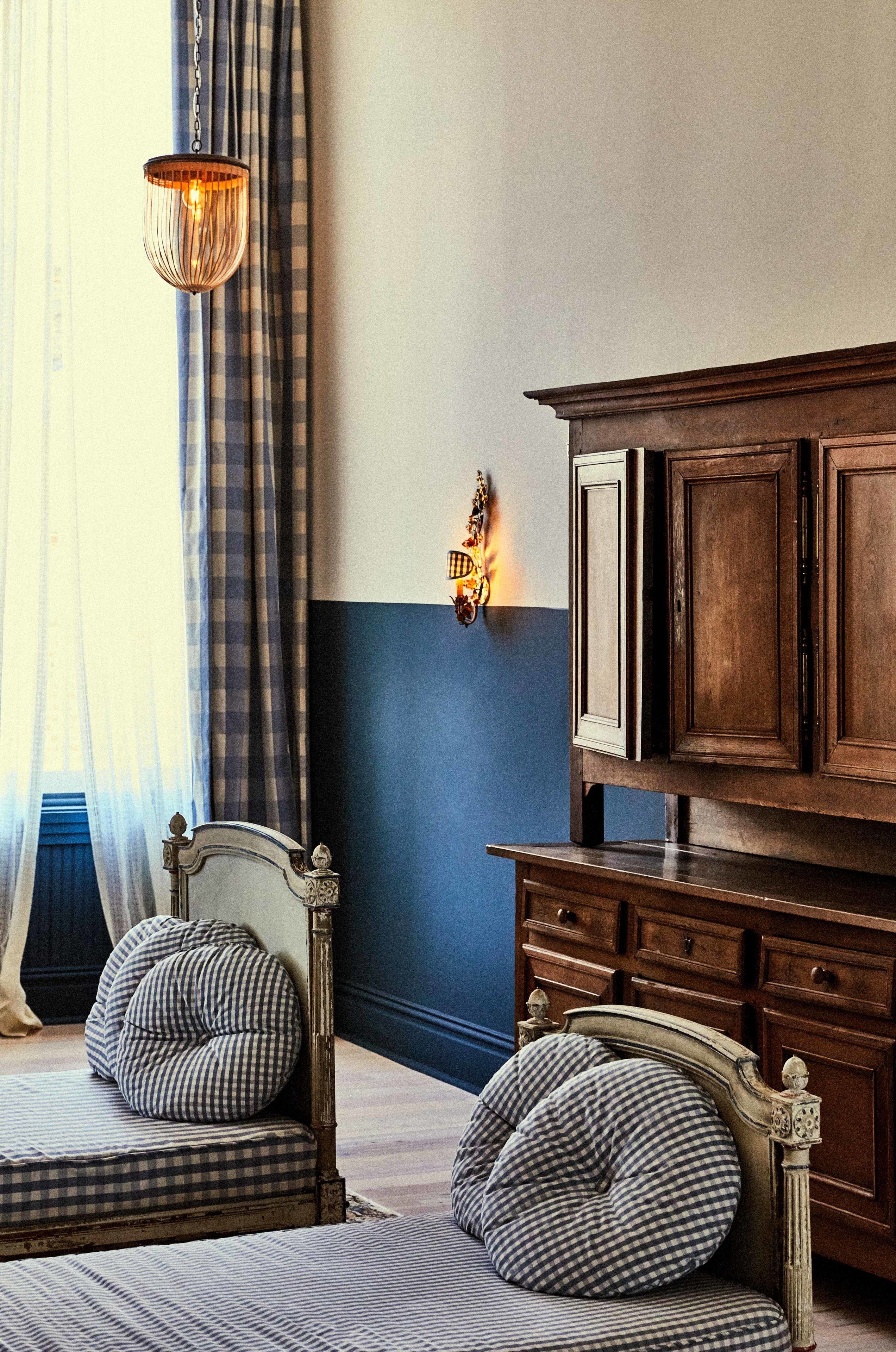 A bedroom with a checkered bedspread, a wooden dresser, and a hanging light fixture.