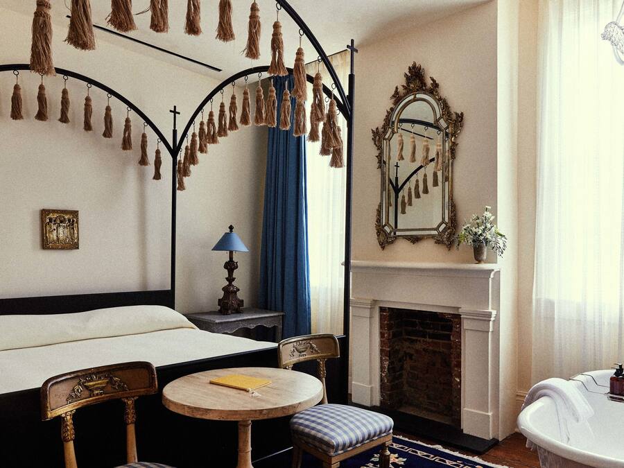 Quarto com cama de dossel, lareira, espelho e mesa redonda pequena.