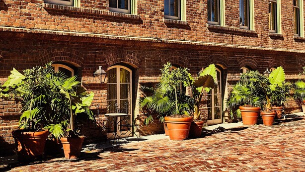 A brick building with multiple windows and a paved courtyard with potted plants. - Hotel Peter and Paul, an Ash Hotel (New Orleans)