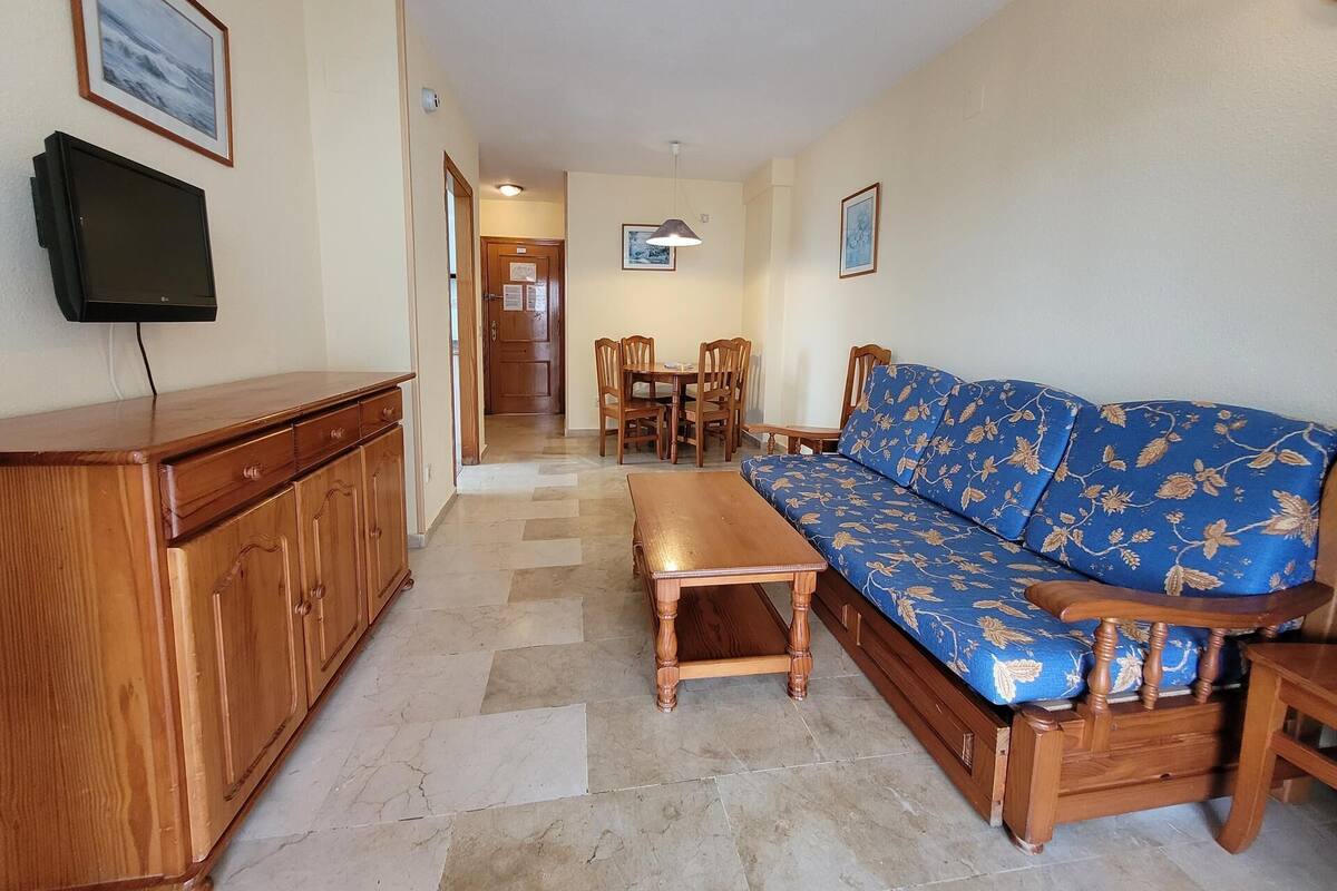 A living room with a sofa, wooden cabinet, TV, and a dining area with chairs and a table.