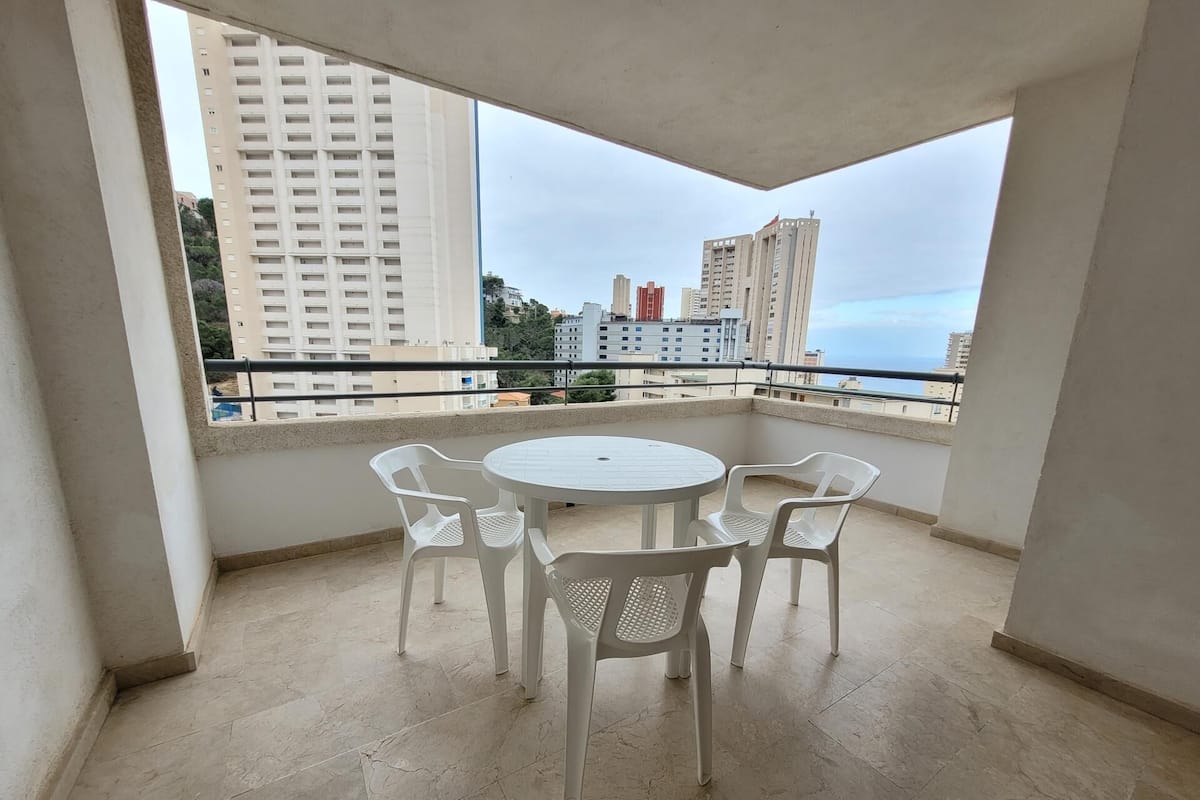 A balcony with a round table and four chairs, overlooking a cityscape with tall buildings.