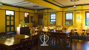 A hotel dining area with multiple tables and chairs, an exit sign, and air conditioning units. - Hotel Cunnamulla (Cunnamulla)