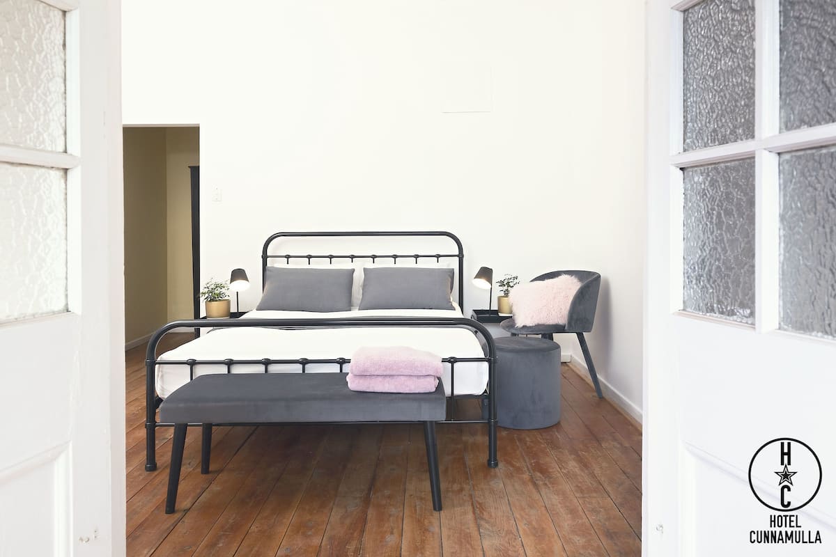 Un dormitorio con estructura metálica para la cama, una mesita de noche con lámpara y un banco.