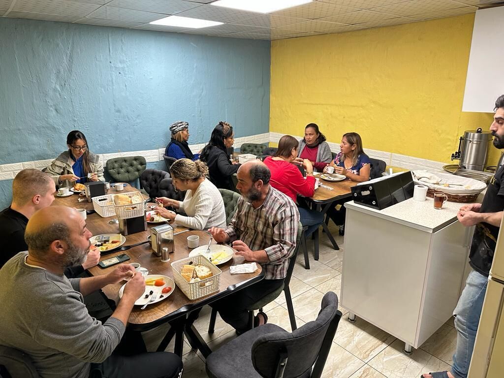 Um grupo de pessoas jantando em um espaço com parede azul e amarela, mesa de buffet e área de cozinha.