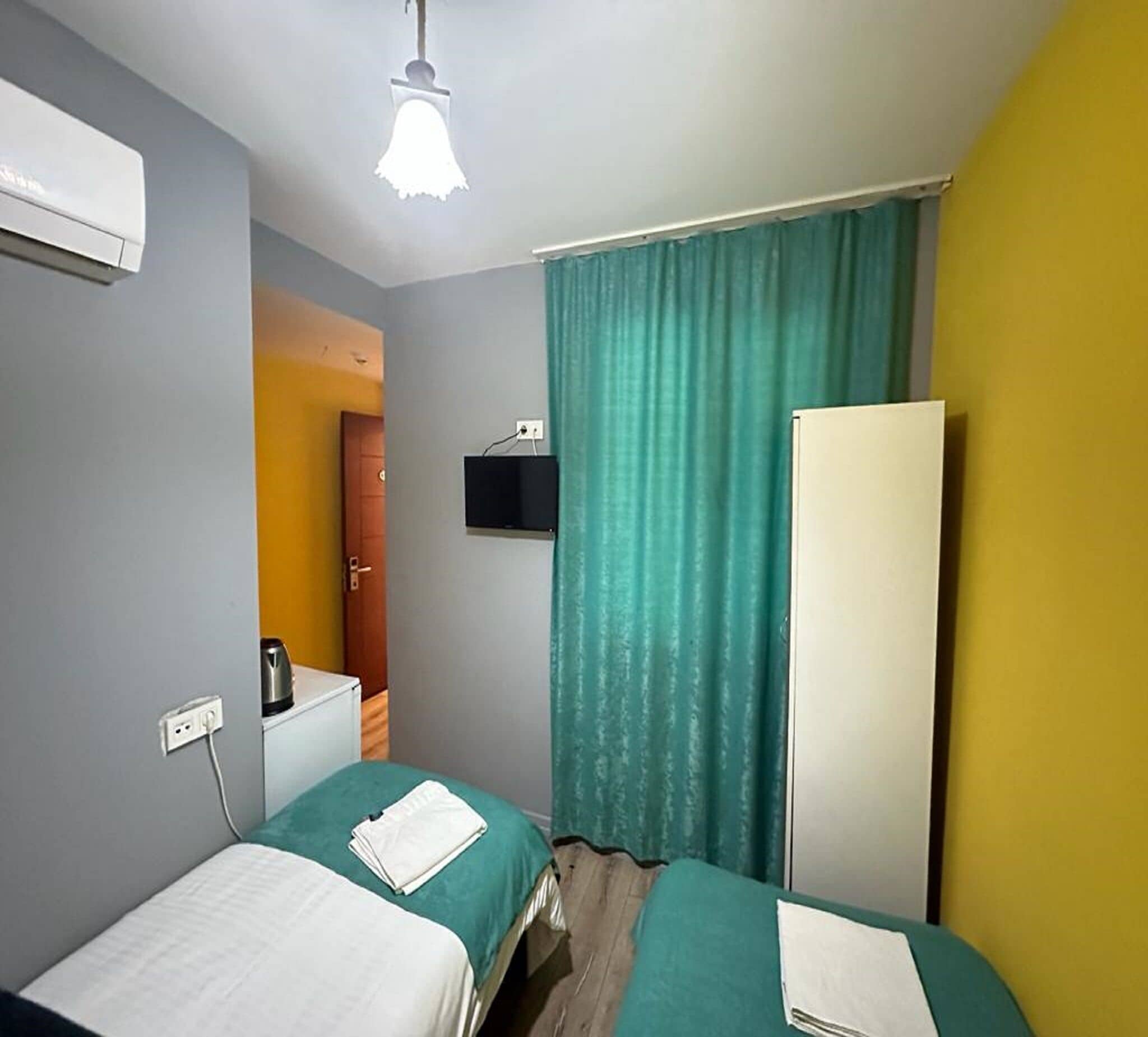 A hotel room with two beds, a TV, an air conditioner, and a window with curtains.