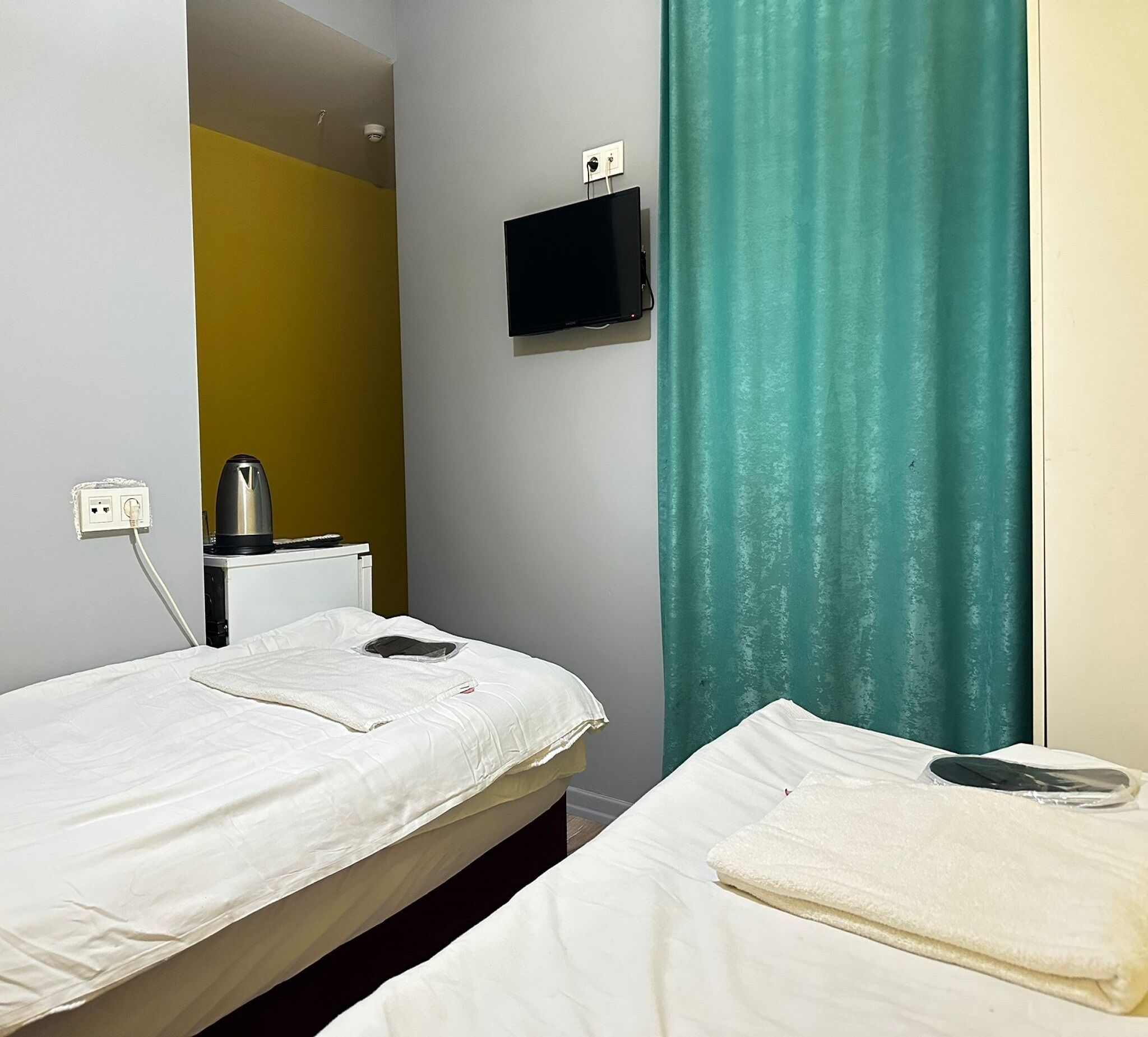 A twin room with two beds, a TV, a kettle, and a curtain.