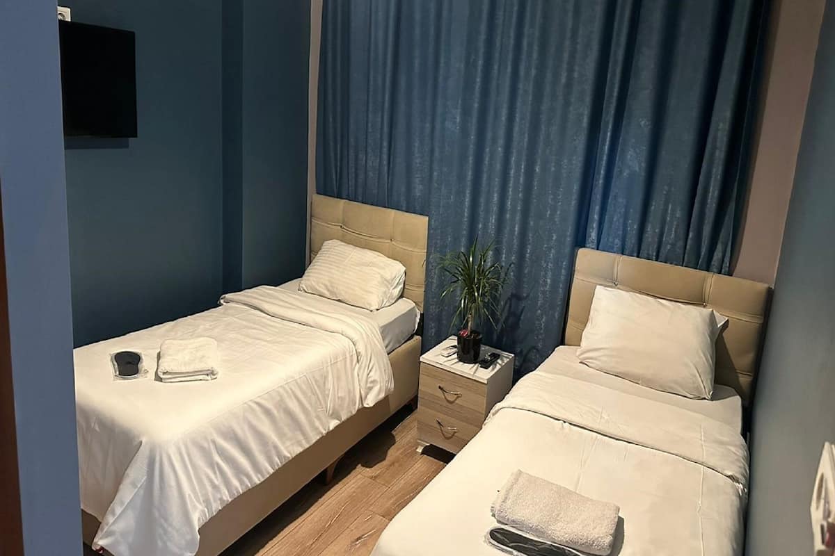 A hotel room with two beds, a nightstand, a potted plant, and a TV mounted on the wall.