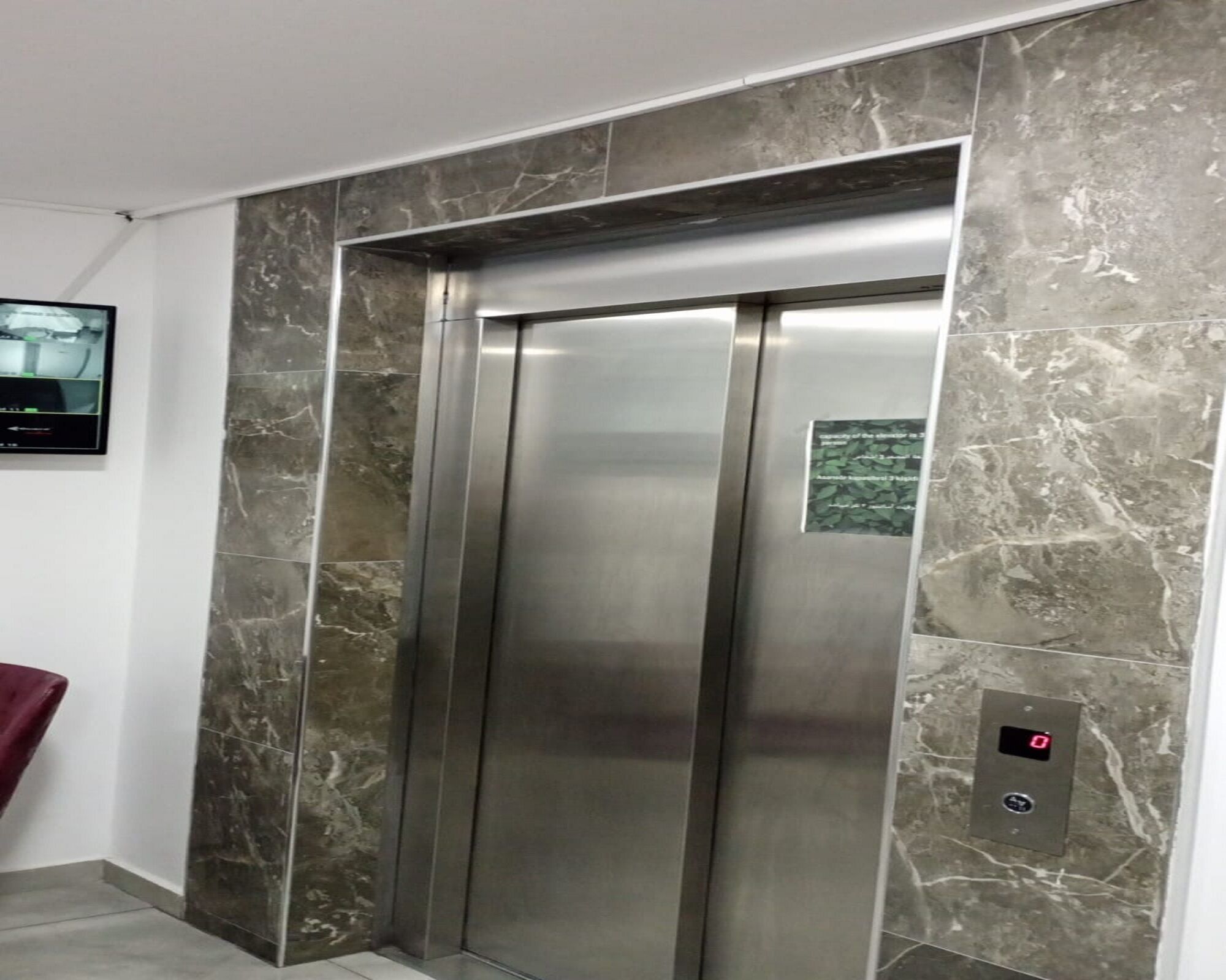 Um elevador moderno com acabamento em aço inoxidável, paredes revestidas de mármore e painel de exibição digital.