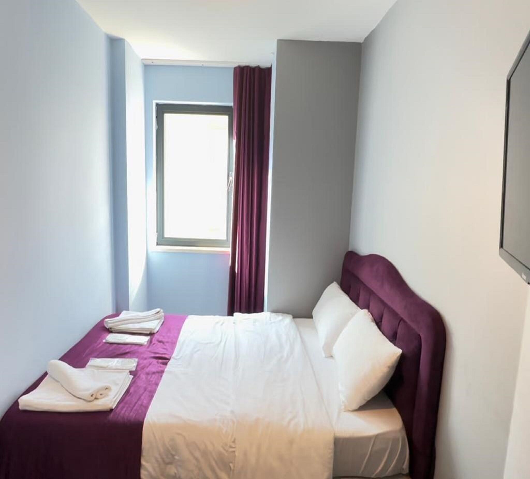 A hotel room with a bed, a window with curtains, and a view of the outside.