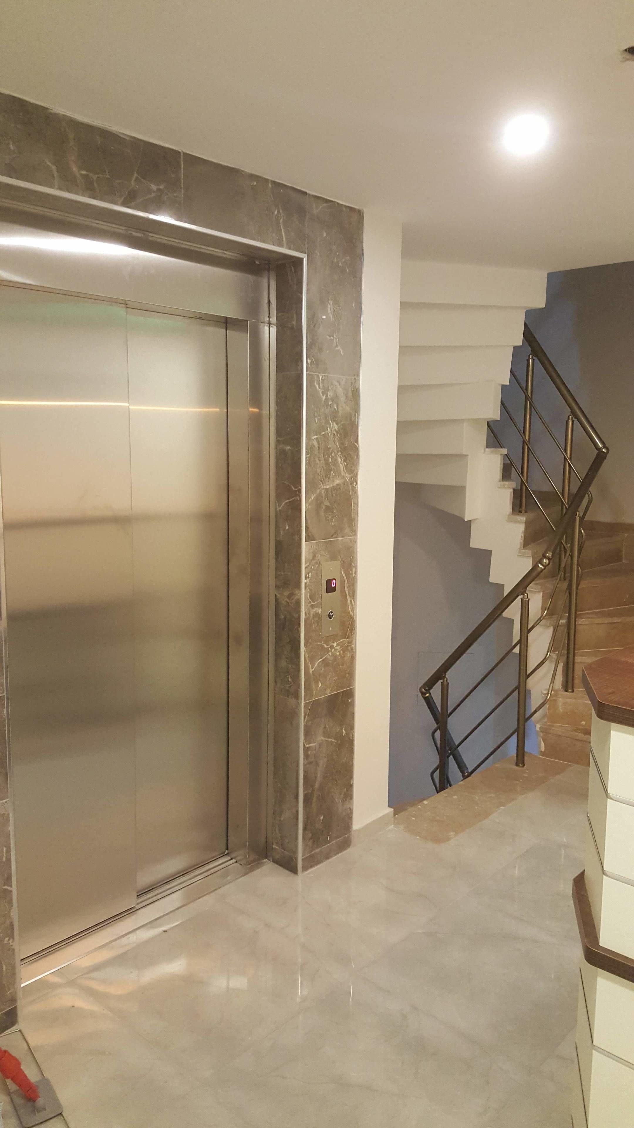 Um elevador com acabamento em mármore, uma escadaria com corrimãos de metal e piso em azulejo.