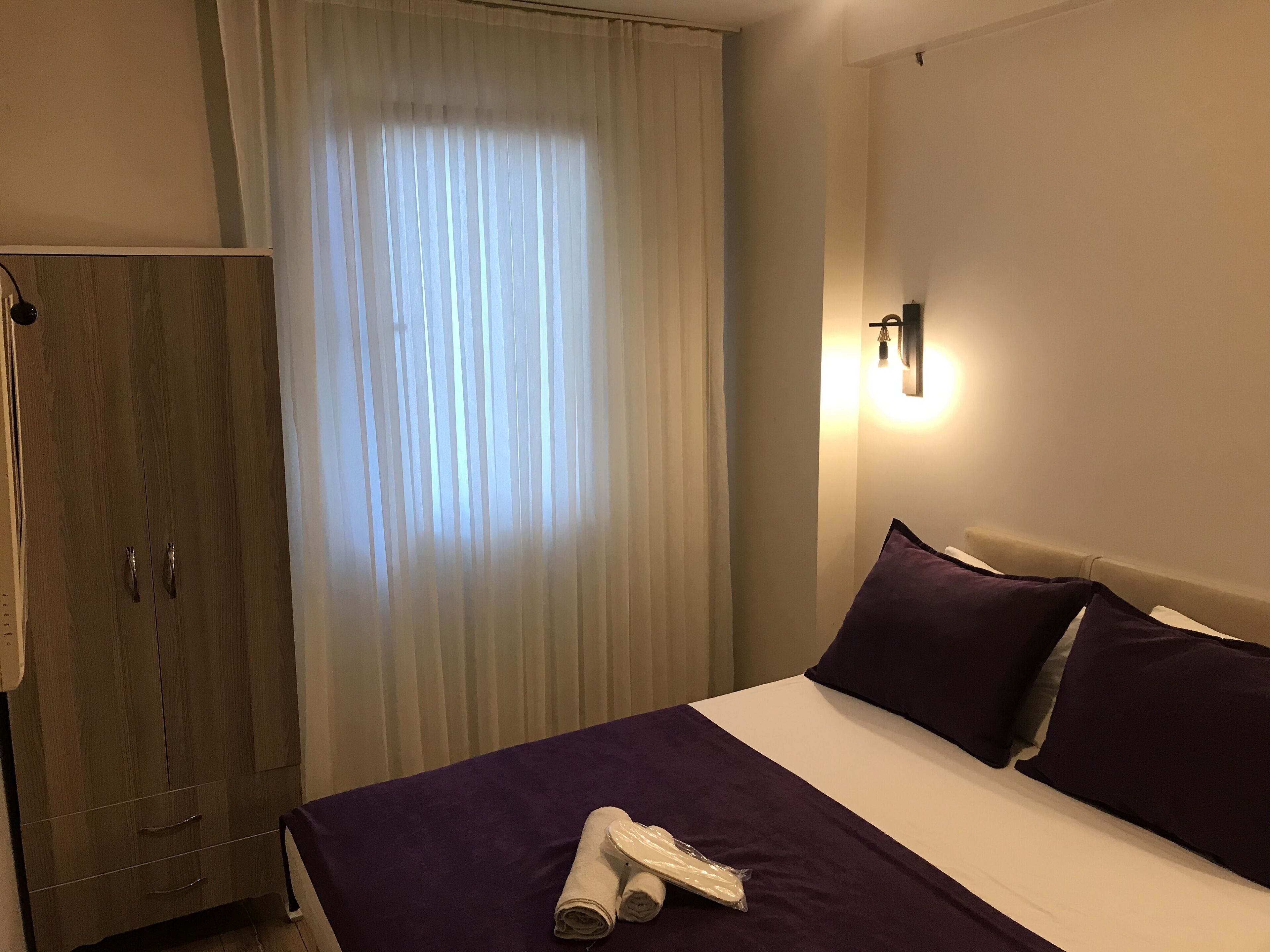 Une chambre d’hôtel avec un lit, une armoire et une fenêtre avec des rideaux.