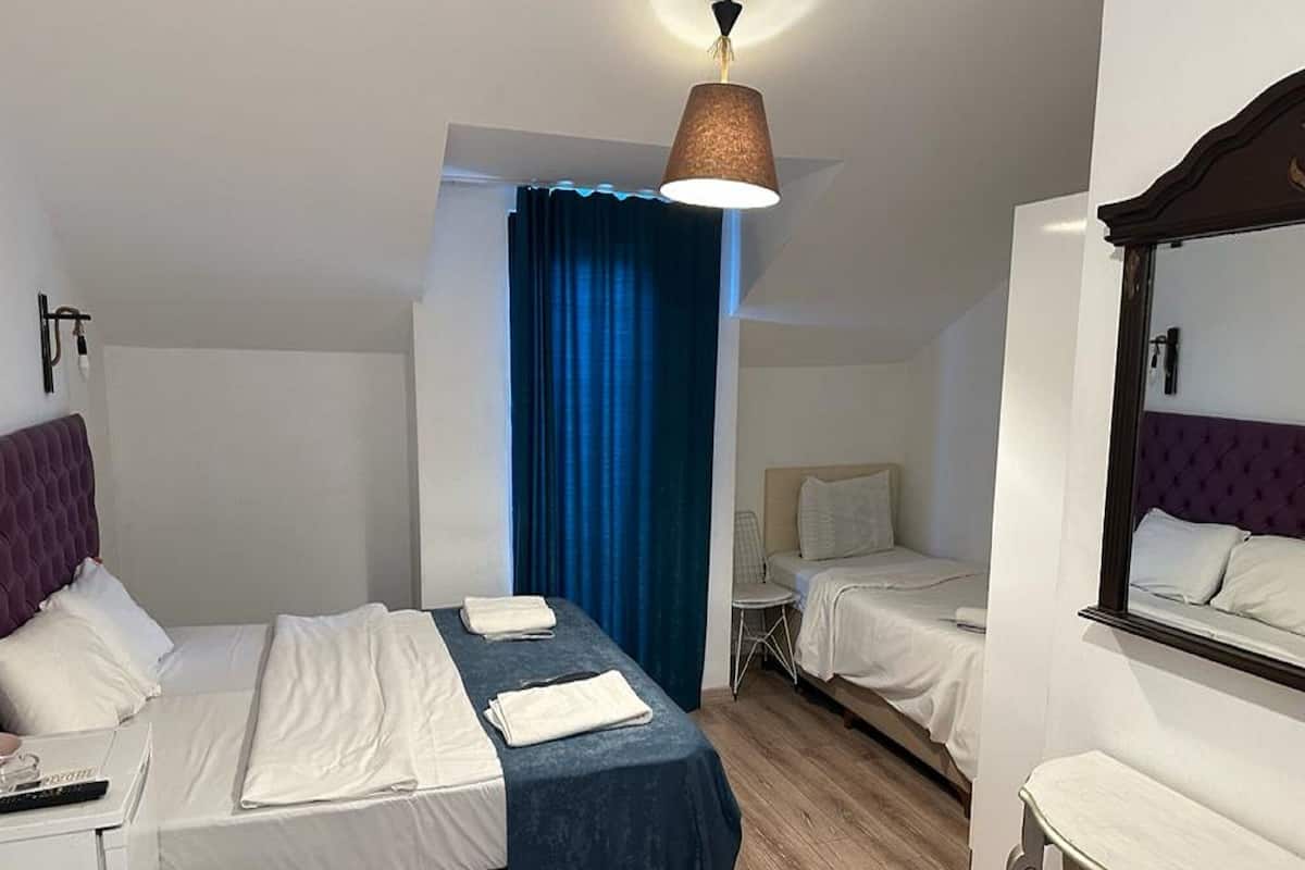 A hotel room with two beds, a desk, a chair, a mirror, and a hanging lamp.
