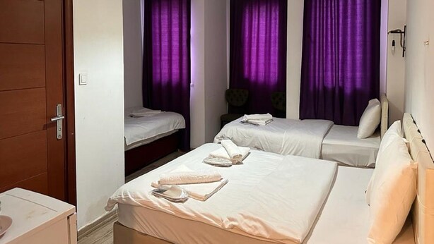 A hotel room with two beds, a wooden door, a small table, and purple curtains. - Taksim Soushian Hotel (Istanbul)