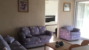 A living room with a sofa, a coffee table, and a chair. There is a ceiling fan and a window with curtains.