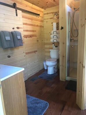 A wooden cabin bathroom with a toilet, a shower, and towels hanging on the wall.