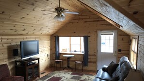 Un intérieur de chalet chaleureux avec un téléviseur, un canapé en cuir et un ventilateur de plafond.