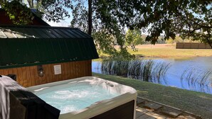Un bain à remous doté d’une terrasse en bois, entouré d’un étang et d’arbres.