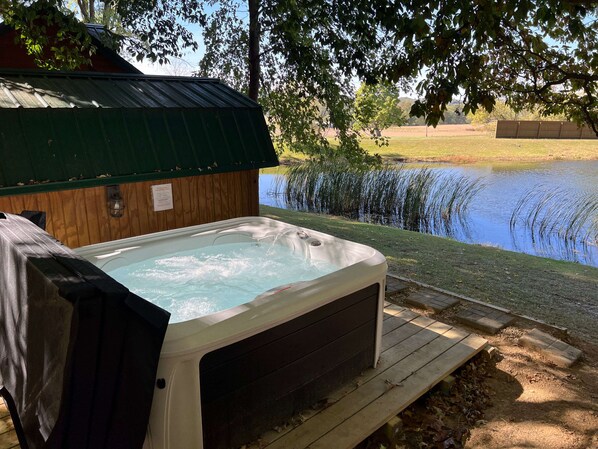 A hot tub with a wooden deck, surrounded by a pond and trees.