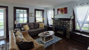 Un salón con sofá, una mesa de centro, chimenea y vistas al exterior.