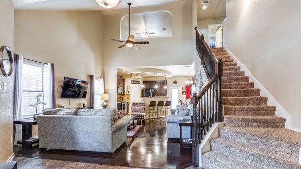 Ein geräumiges Wohnzimmer mit einem großen grauen Sofa, einem Essbereich mit Stühlen, einer Küche im Hintergrund und einer Treppe mit Teppichstufen.