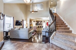 A spacious living room with a large gray sofa, a dining area with chairs, a kitchen in the background, and a staircase with carpeted steps. - Beautiful and cozy home near Sea World 4 mi, Lackland 8 miles, Six Flags14 mi (San Antonio)
