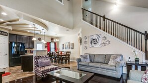 Ein geräumiges Wohnzimmer mit einer Couch, einem Couchtisch und einem gemusterten Sessel. Eine Treppe führt auf eine höhere Ebene.