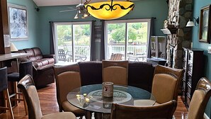 En spiseplads med et rundt glasbord, læderstole, en bar med barstole og en stengulv skorsten.