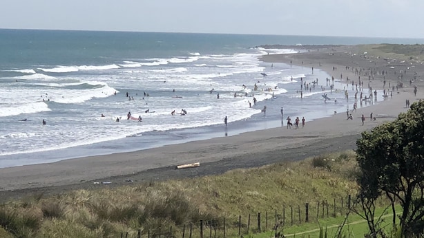 Una playa con olas, gente y una valla.