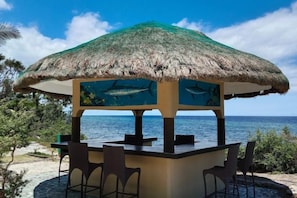 A beachside bar with a thatched roof, seating, and a view of the ocean. - Cabilao Sunset Dive and Beach Resort (Loon)