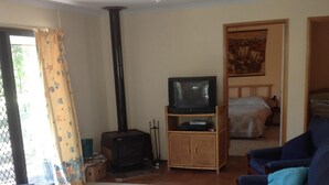 Olohuoneessa on sohva, nojatuoleja, sohvapöytä, puinen tv-taso, jossa on televisio, takka ja seinällä taulu.