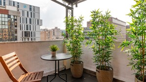 Un balcon avec une chaise en bois, une petite table ronde et trois plants de bambou en pot.