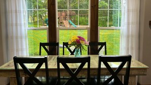 A dining area with a table and chairs, a vase with flowers, and a view of a playground through large windows. -  Both cottages rent as one unit,  Enjoy Privacy & Comfort, Very Family friendly (Branson)